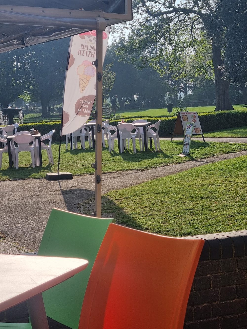 The view out from under the cafe canopy past a red and green chair onto the park path