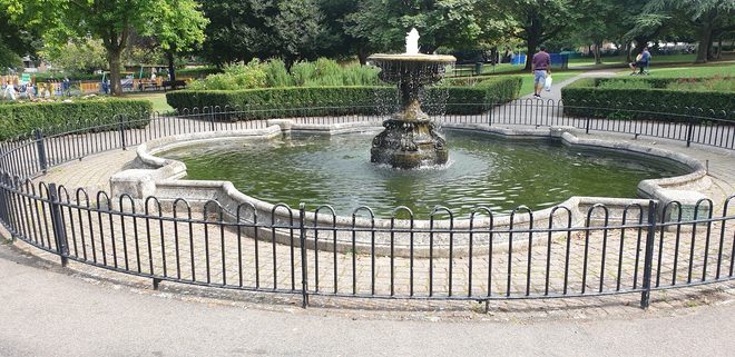The ornamental stone fountain and pond in Manor Park, enclosed by black railings